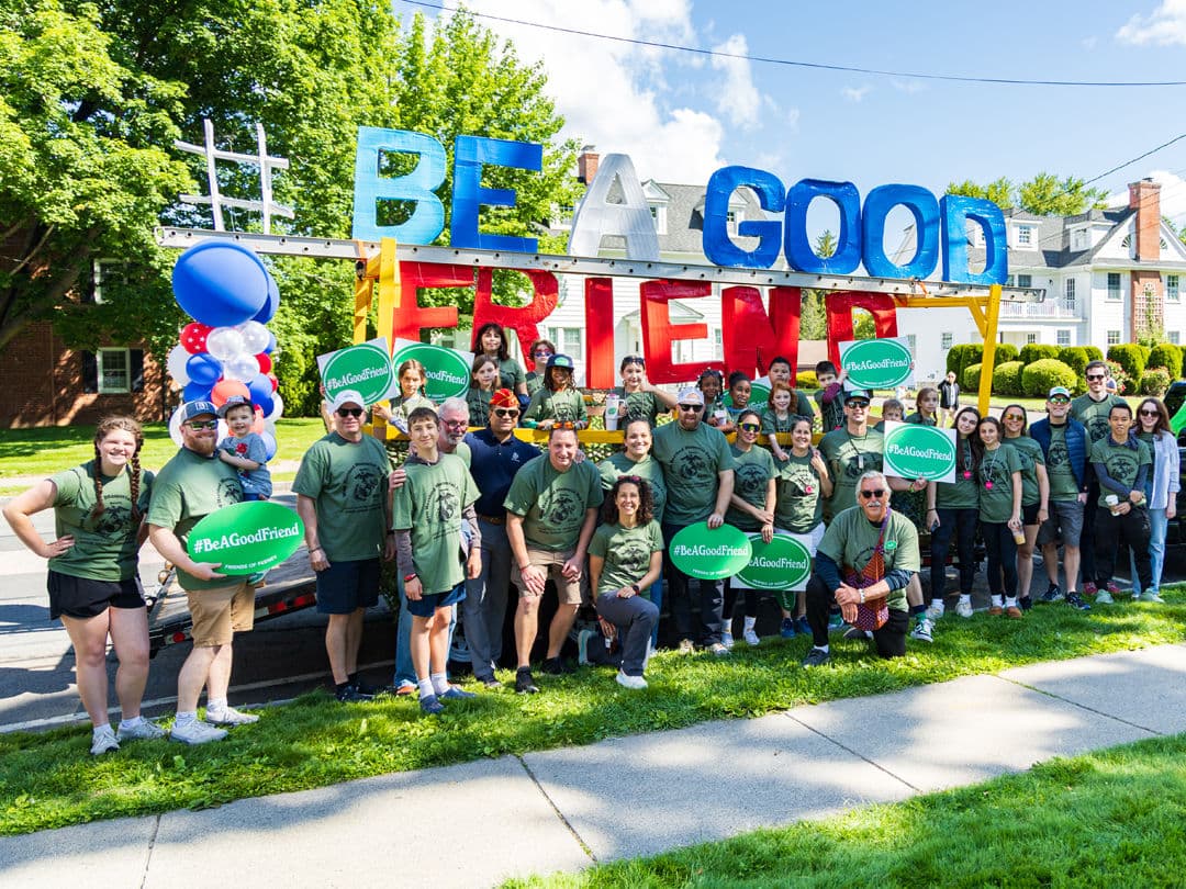 Friends of Feeney marchers in matching green shirts holding #BeAGoodFriend signs beside the red, white and blue float