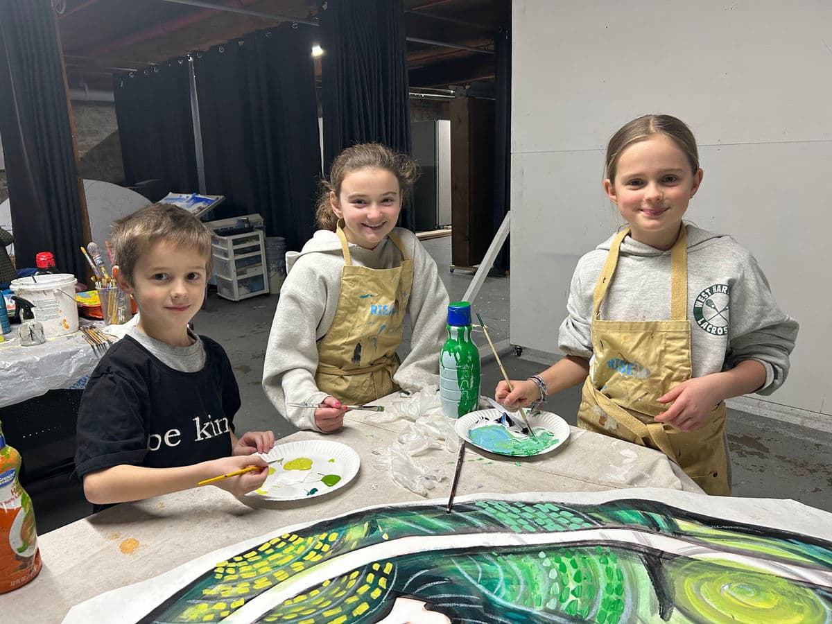 Children with paintbrushes working on the #BeAGoodFriend mural