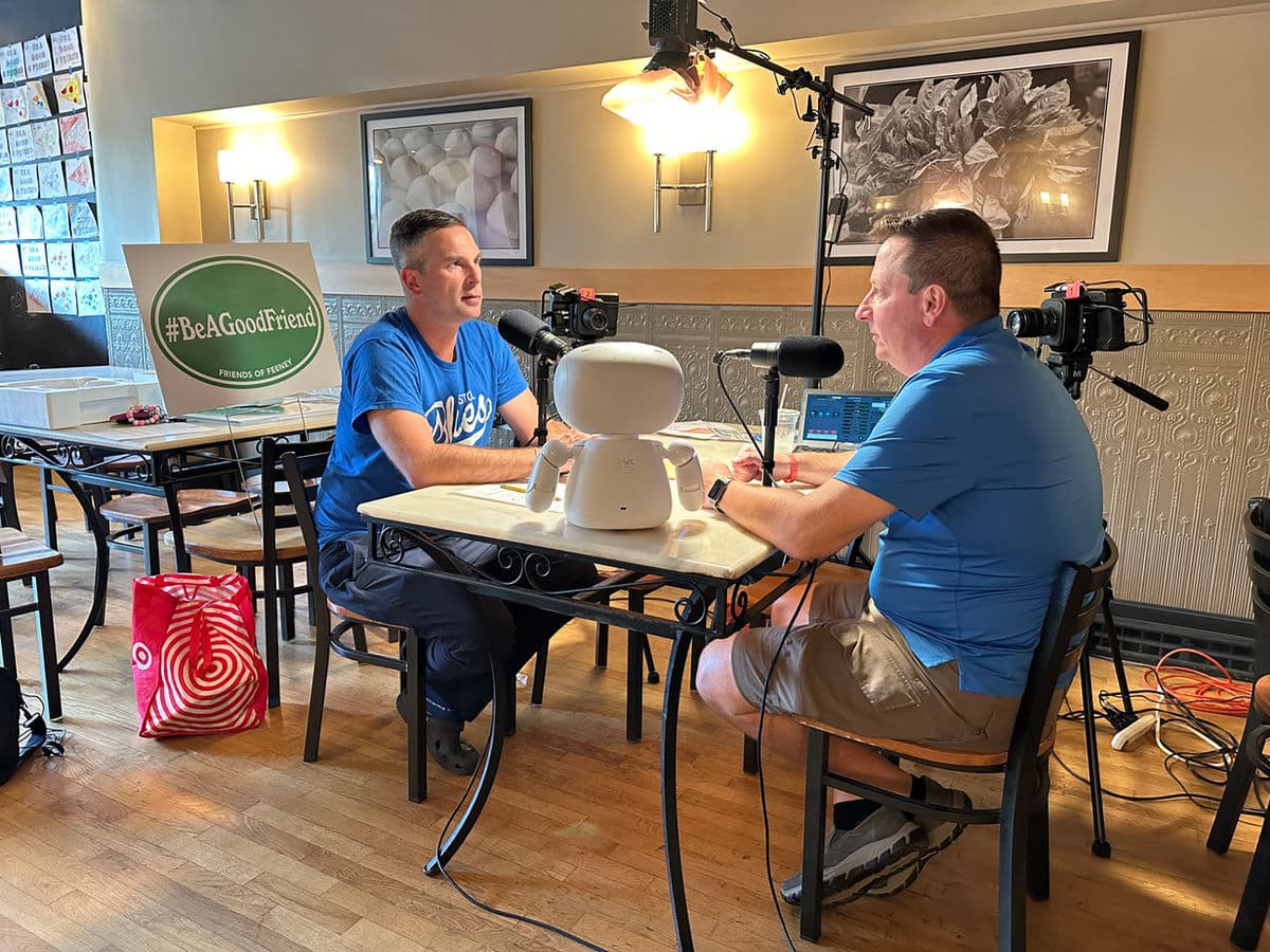 Two men recording an episode of Feeney Talks With Friends at a table set up with microphones and cameras