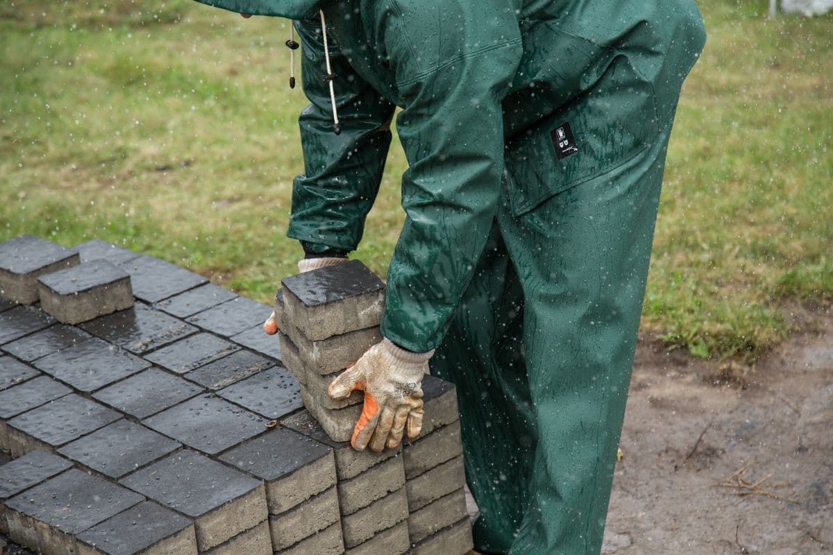 A crew member in rain gear setting concrete pavers by hand