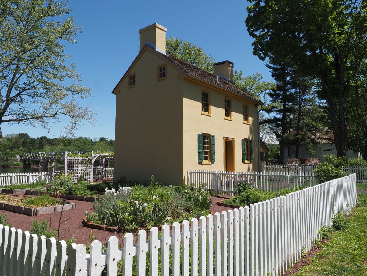 A colonial house with a white picket fence around a kitchen garden of raised beds
