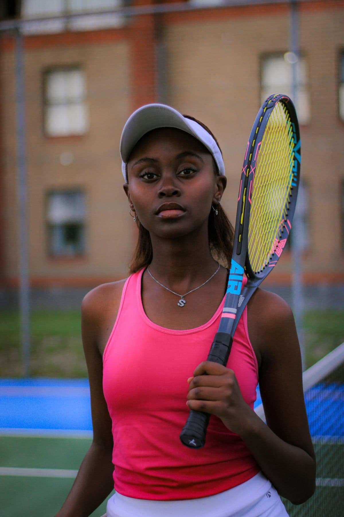 Amara Ellis in a pink tank top and white visor, racket resting on her shoulder