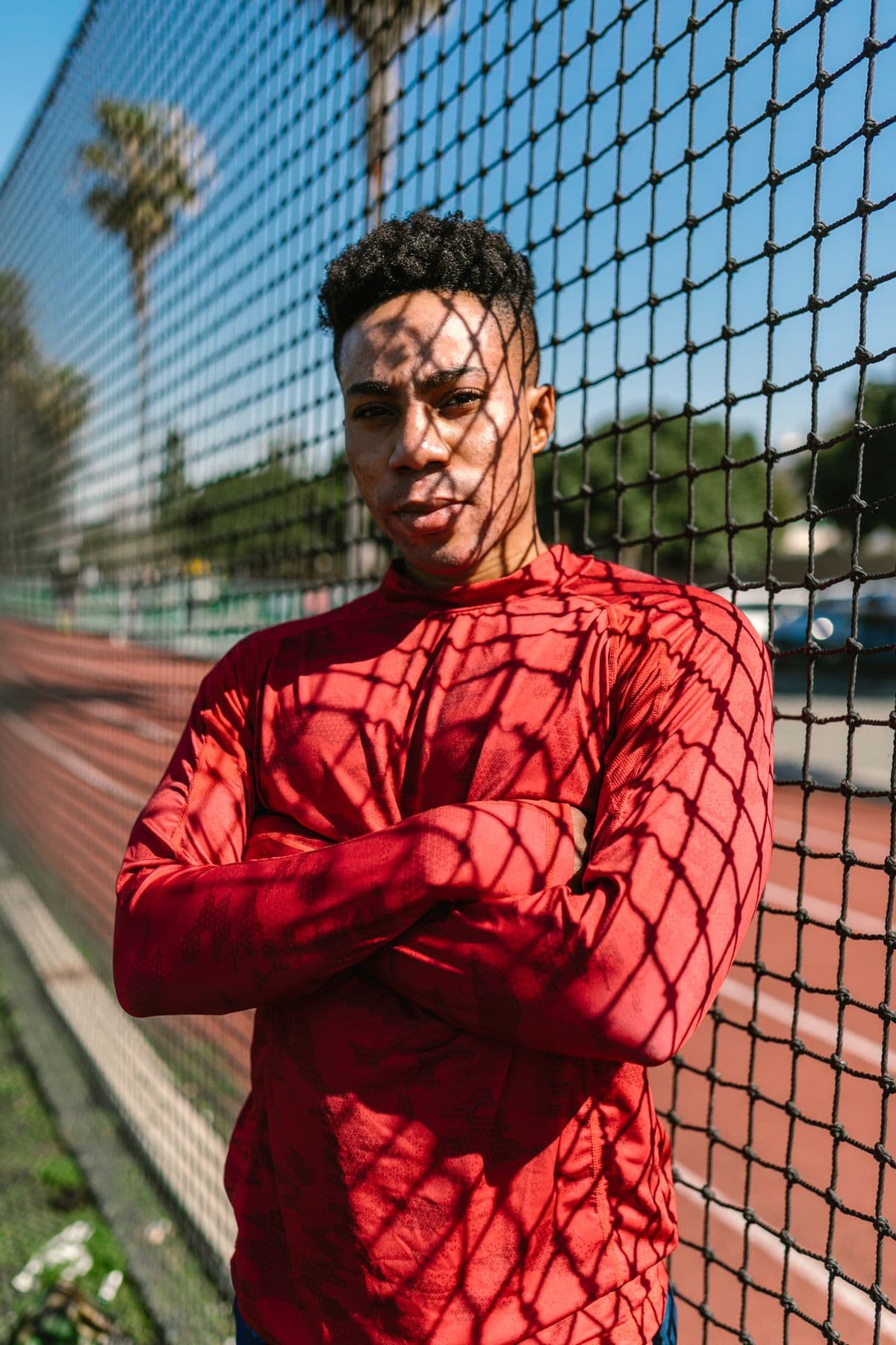 Marcus Reid in a red training top, arms crossed, leaning on a court fence