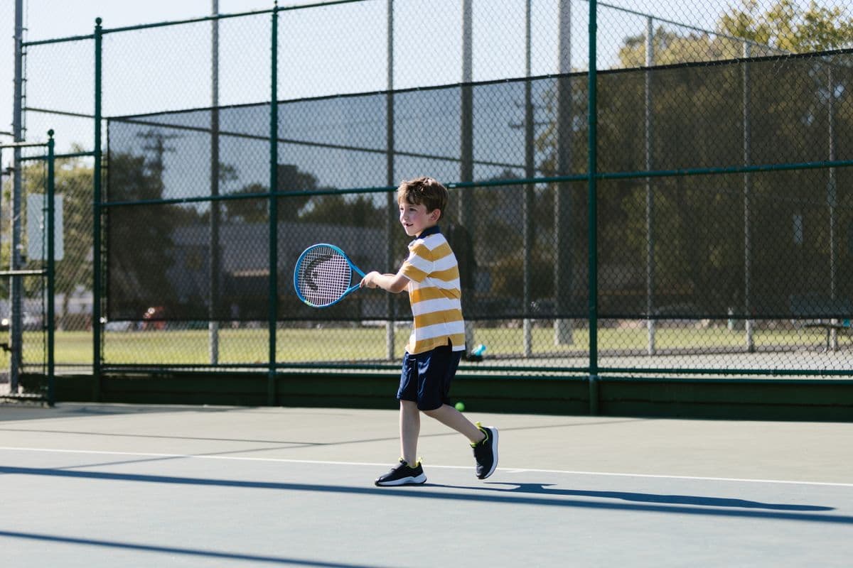A young boy in a striped shirt follows through on a forehand