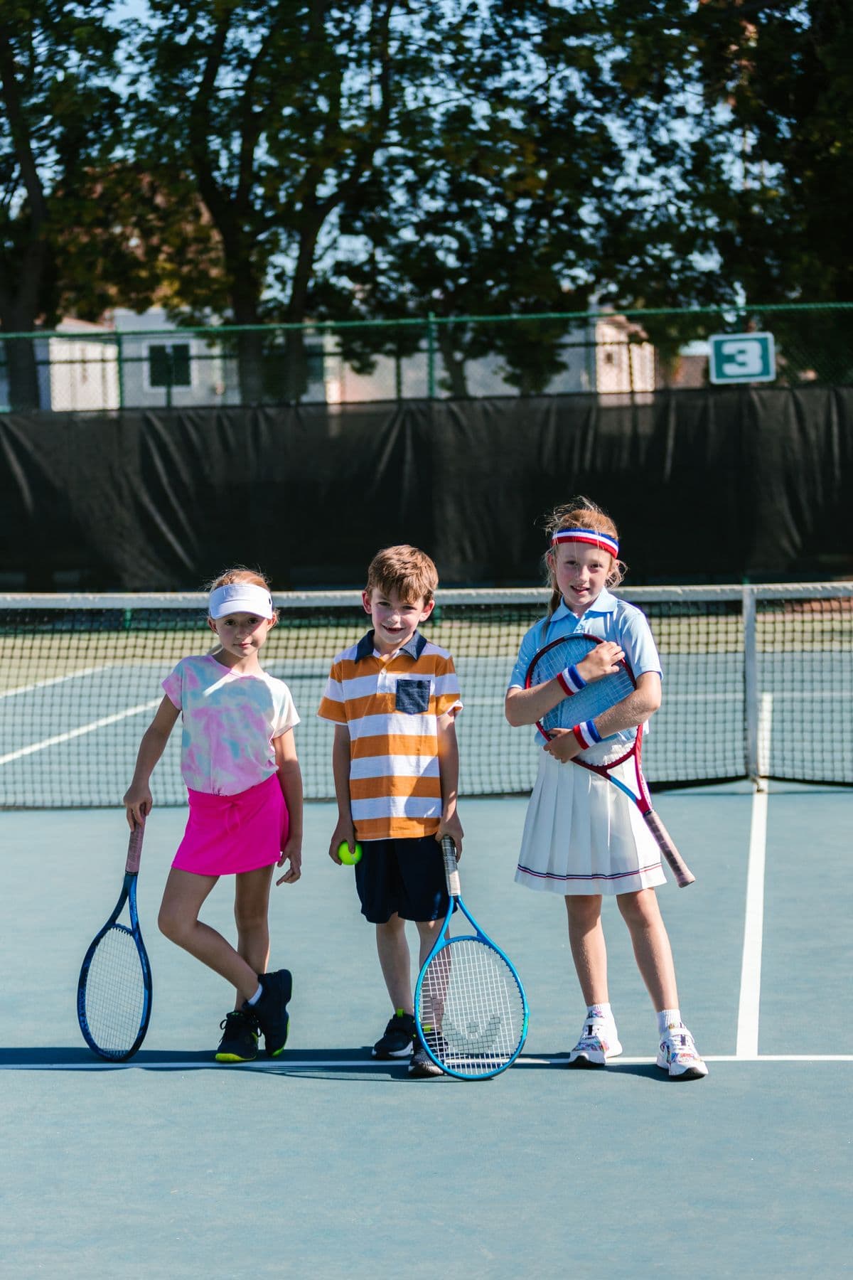 Three young players stand at the net holding their rackets and smiling