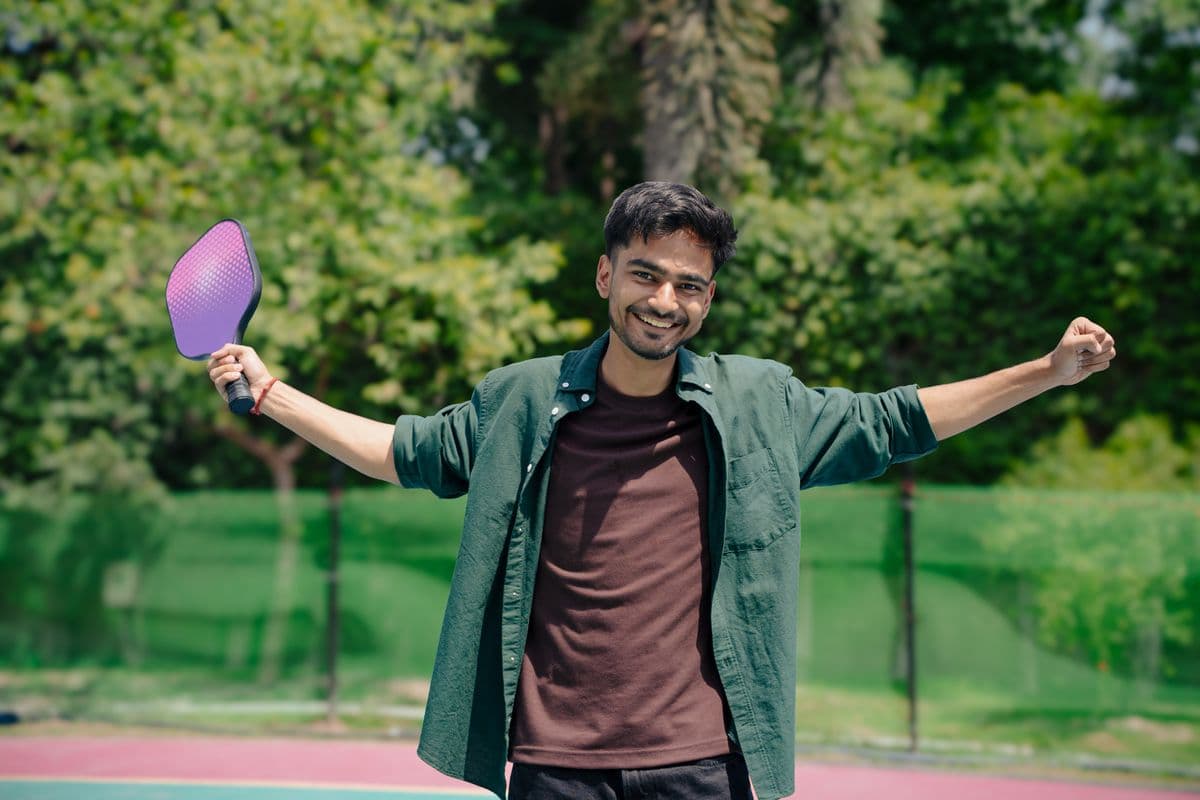 A smiling player throws his arms wide with a purple paddle in one hand