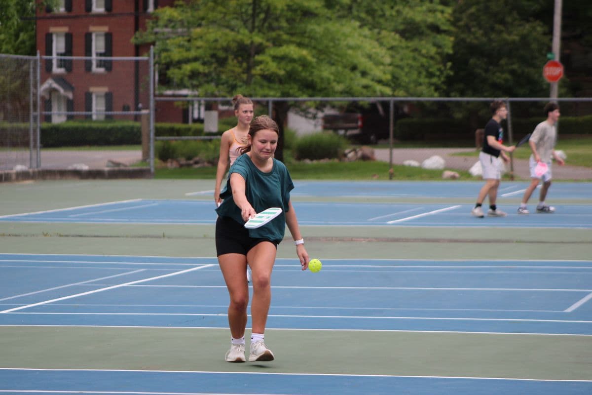 A player hits an underhand serve during a doubles game on blue pickleball courts