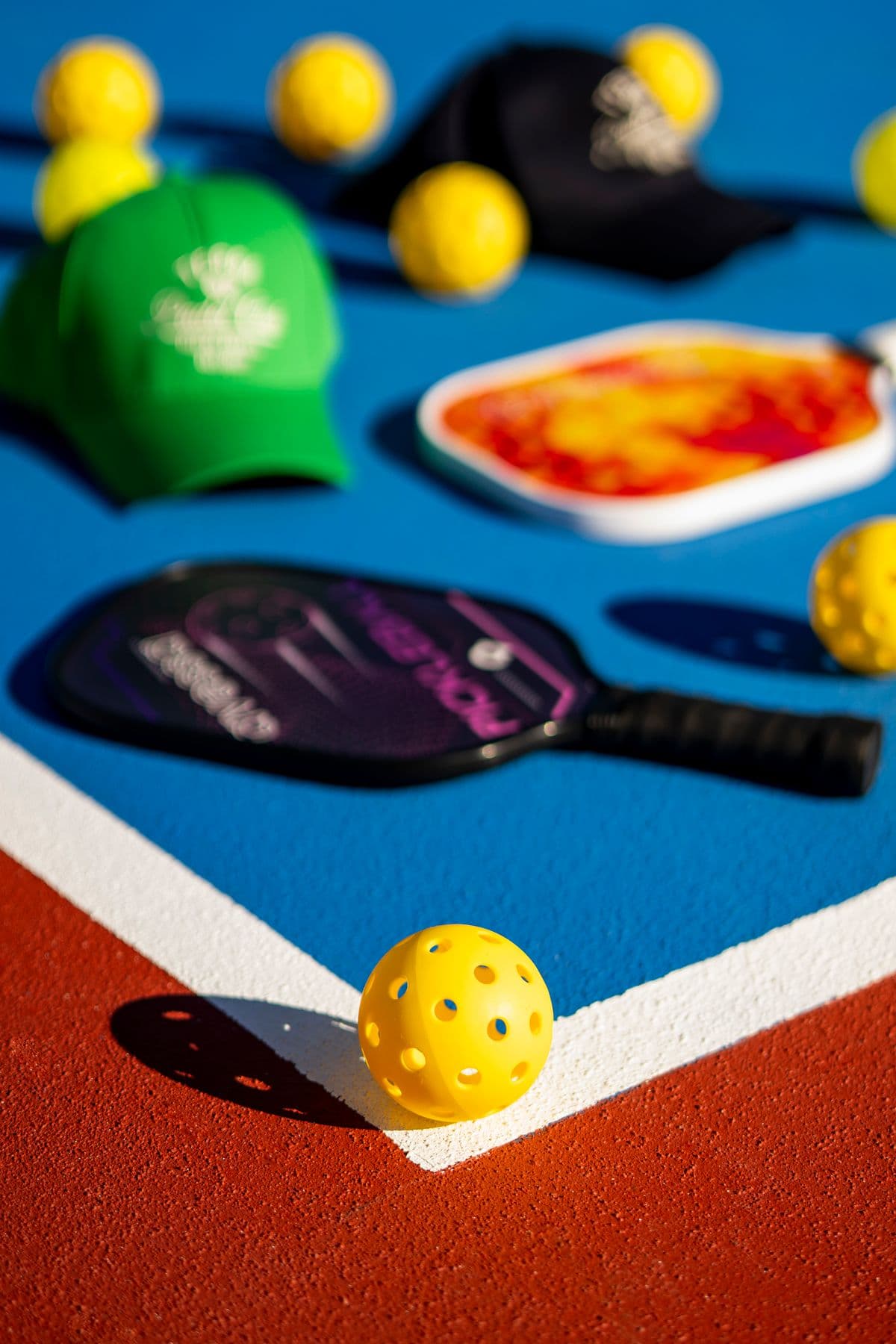 Pickleball paddles, caps and yellow balls on a blue court with a red surround