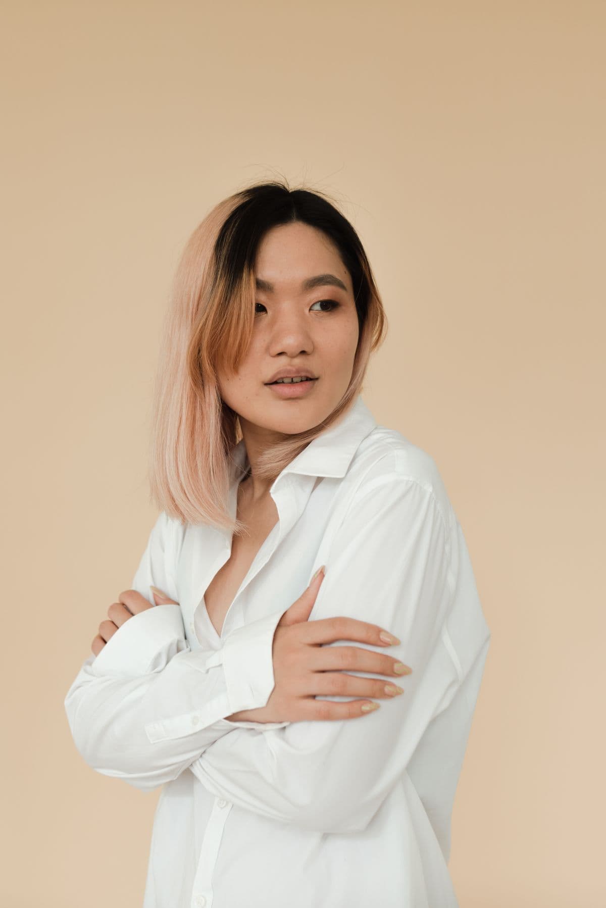 Mina Cho in a white shirt with blush-pink hair against a sand-colored wall