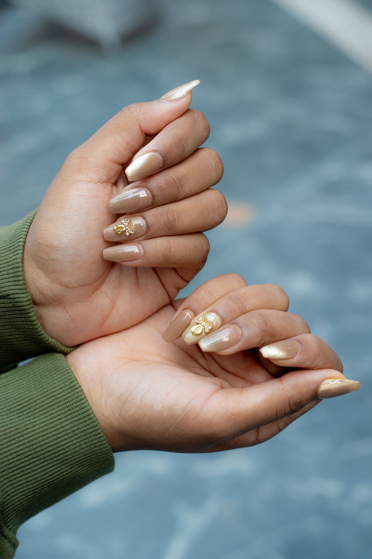 Long coffin nails in caramel gel with gold chrome tips and small gold bow charms