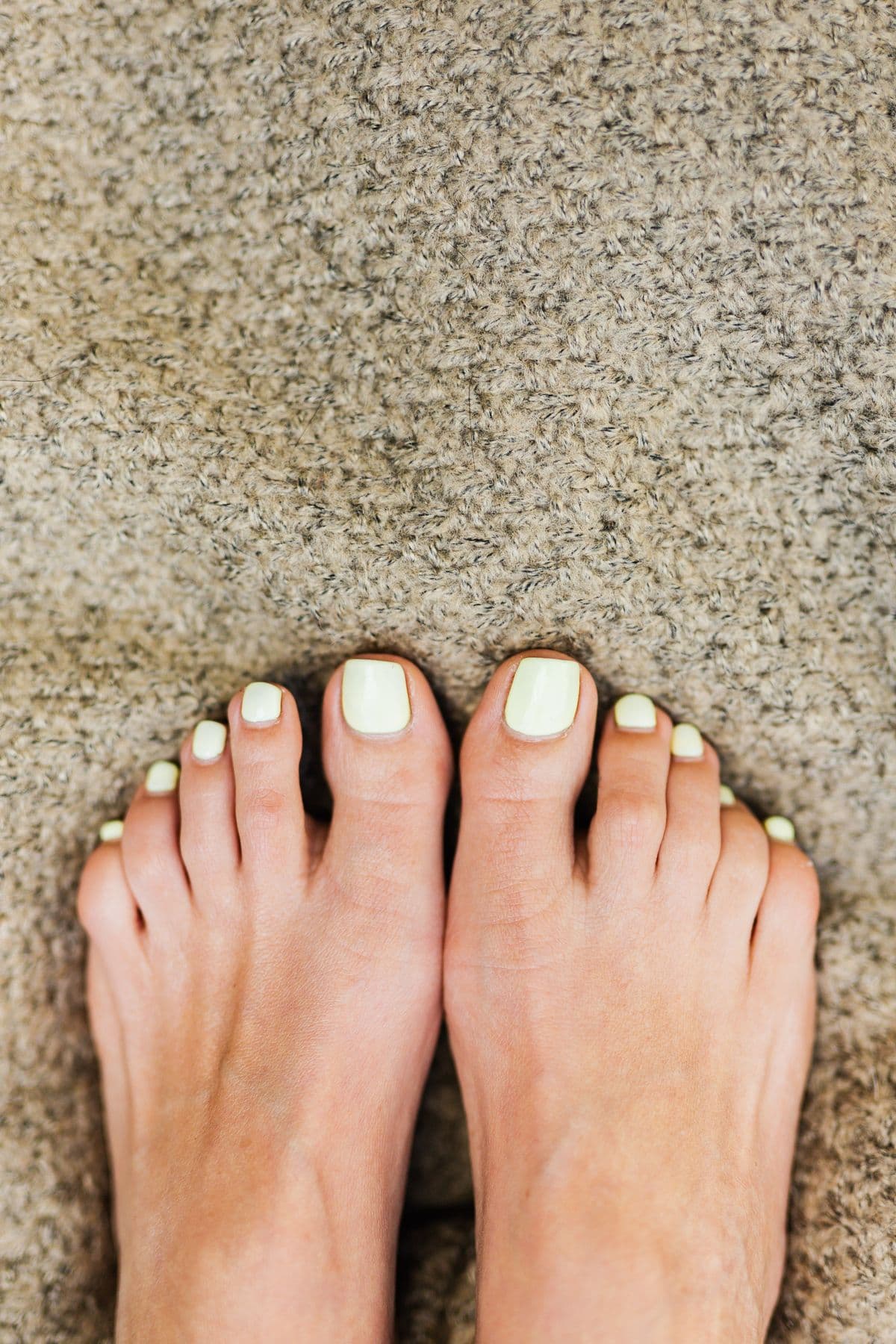 Bare feet on an oatmeal rug with toenails in pale butter-yellow polish