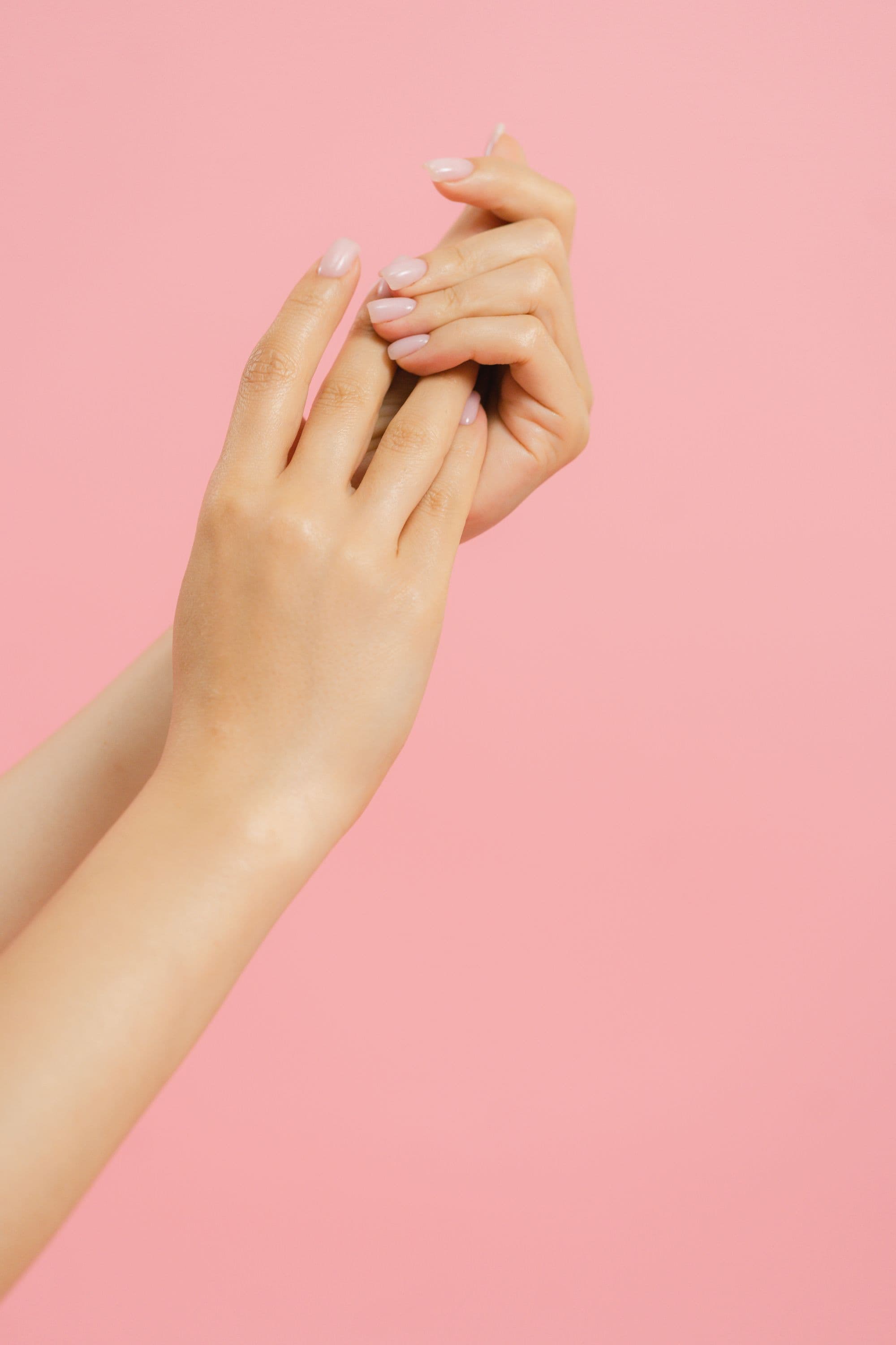 Two raised hands with a glossy milky-pink manicure against a soft pink backdrop