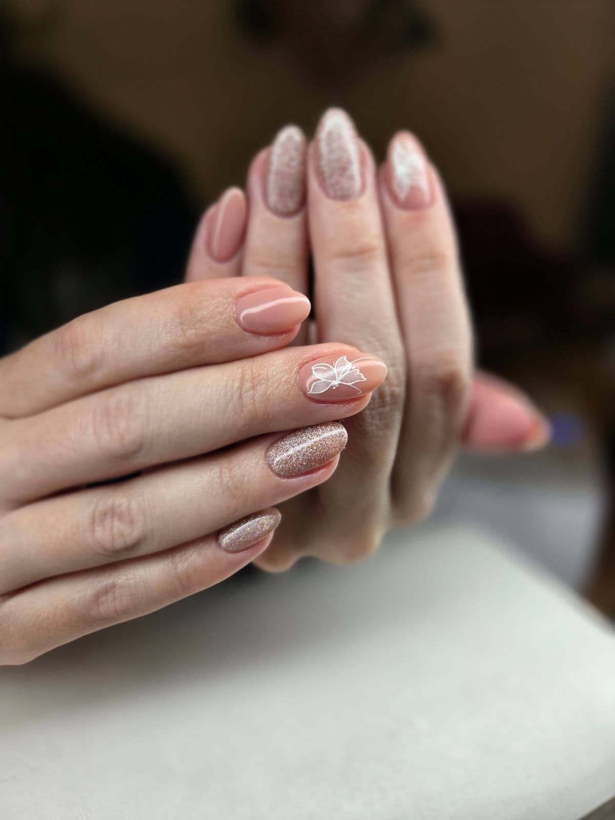 Nude almond nails with rose-gold glitter accents and a hand-painted white butterfly