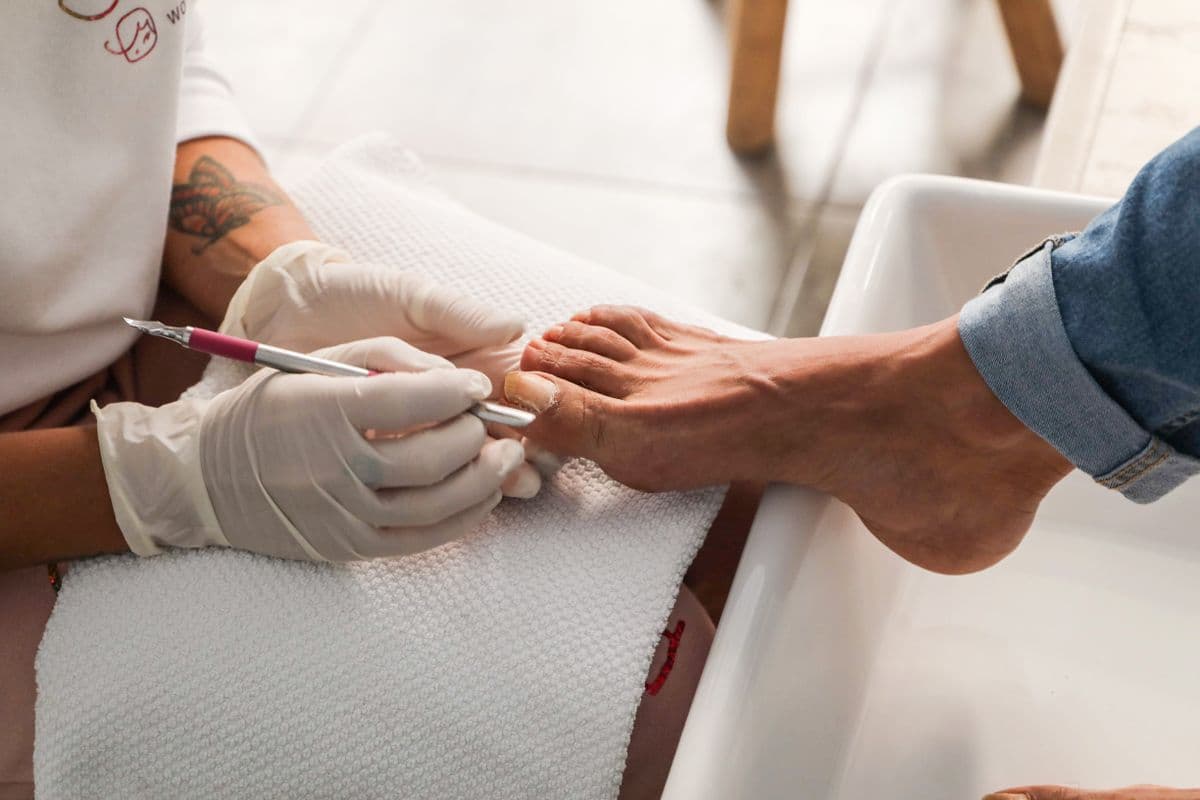 A gloved artist tidying a client’s toenails over a white pedicure basin