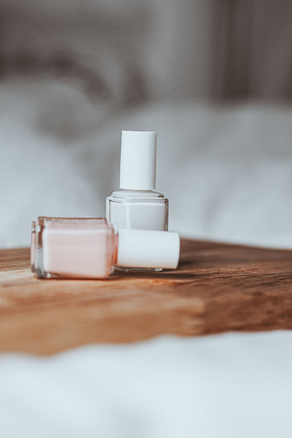 Two bottles of polish, one blush and one milky white, on a wooden tray