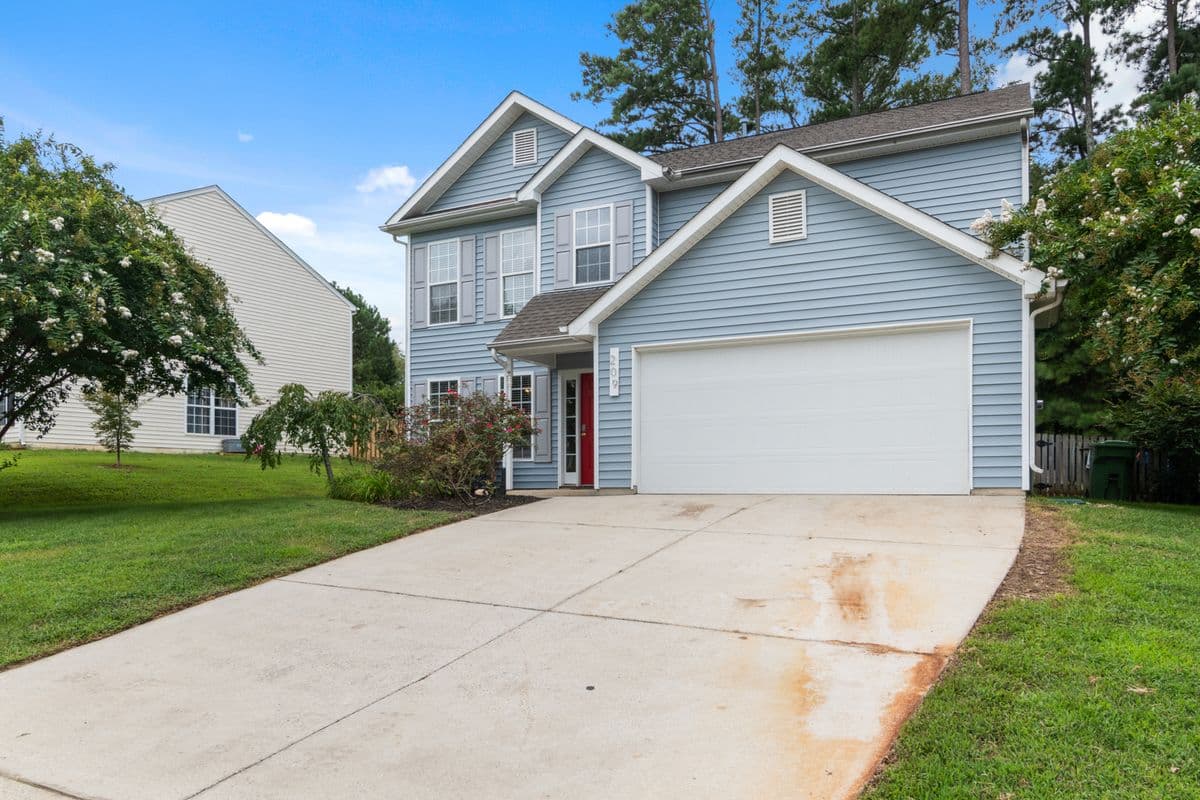 Two-story blue-gray house with a front gable over the garage and a long concrete driveway