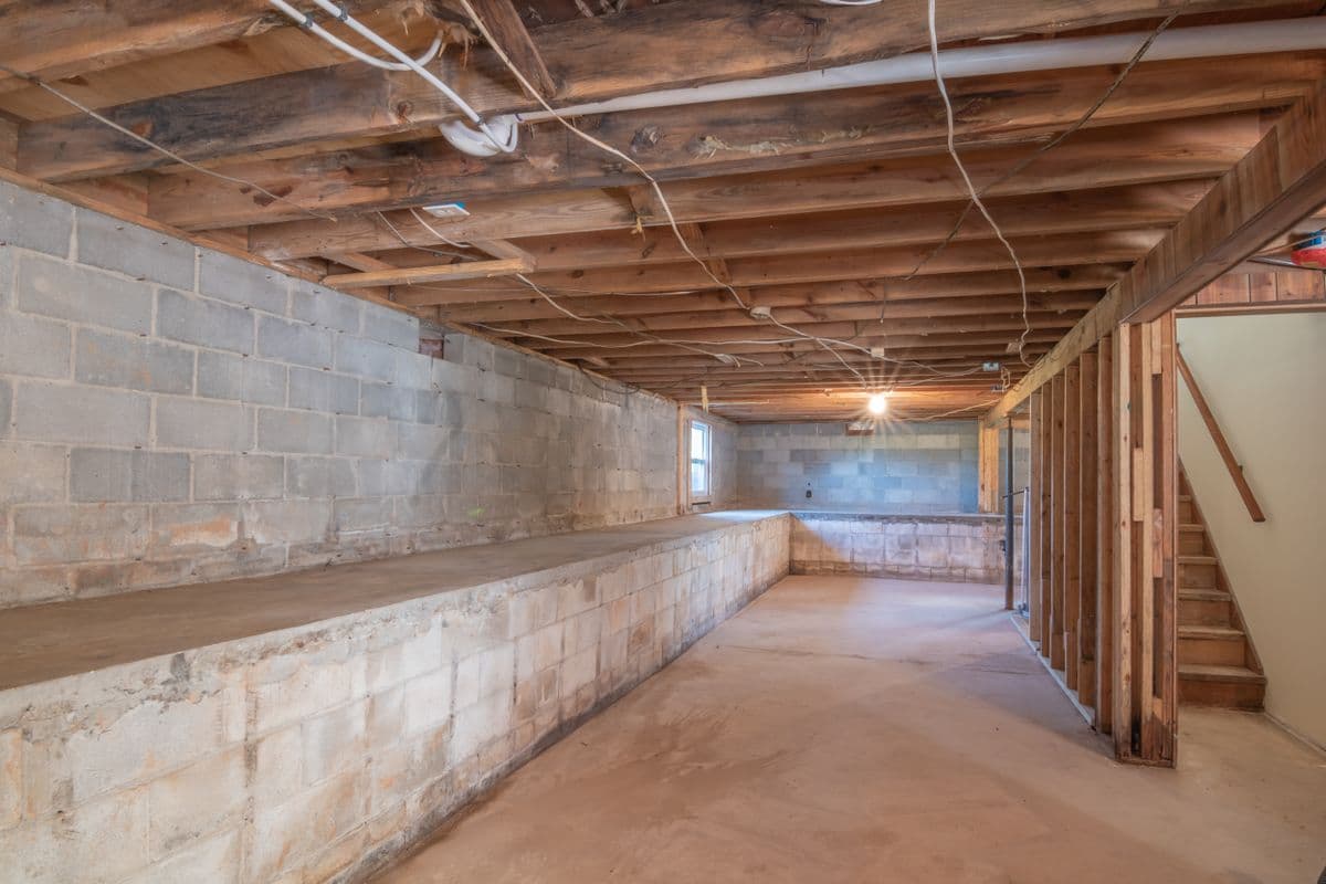Unfinished basement with cinder block walls, exposed joists and a bare concrete floor
