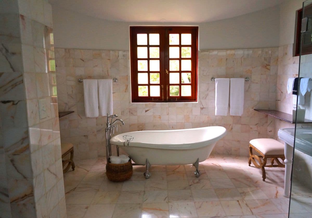Primary bath with a clawfoot soaking tub under a divided-light window and warm marble tile