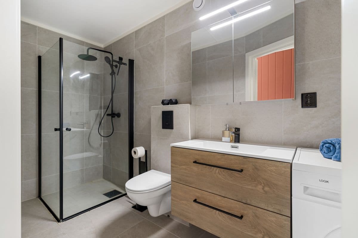 Wood vanity with a matte black frameless shower and large-format gray tile