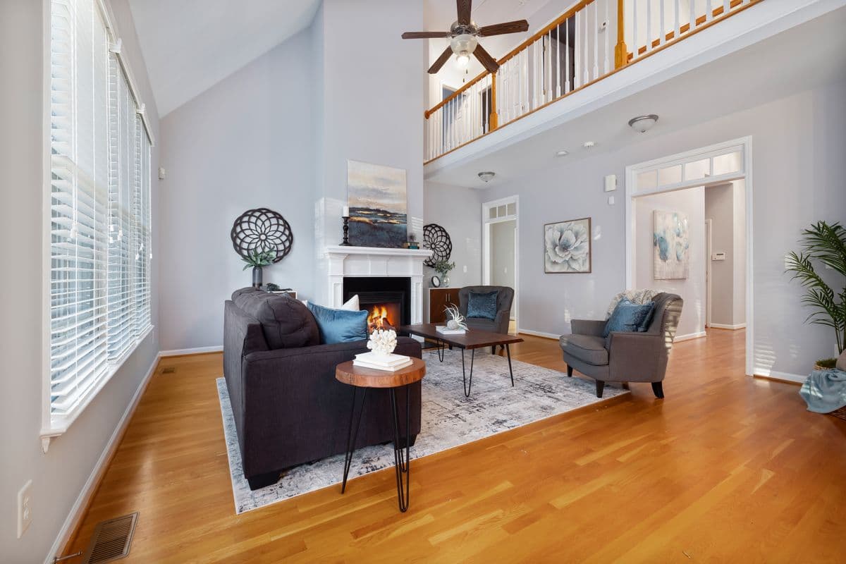 Two-story living room with a fireplace, oak floors, tall windows and a balcony railing above