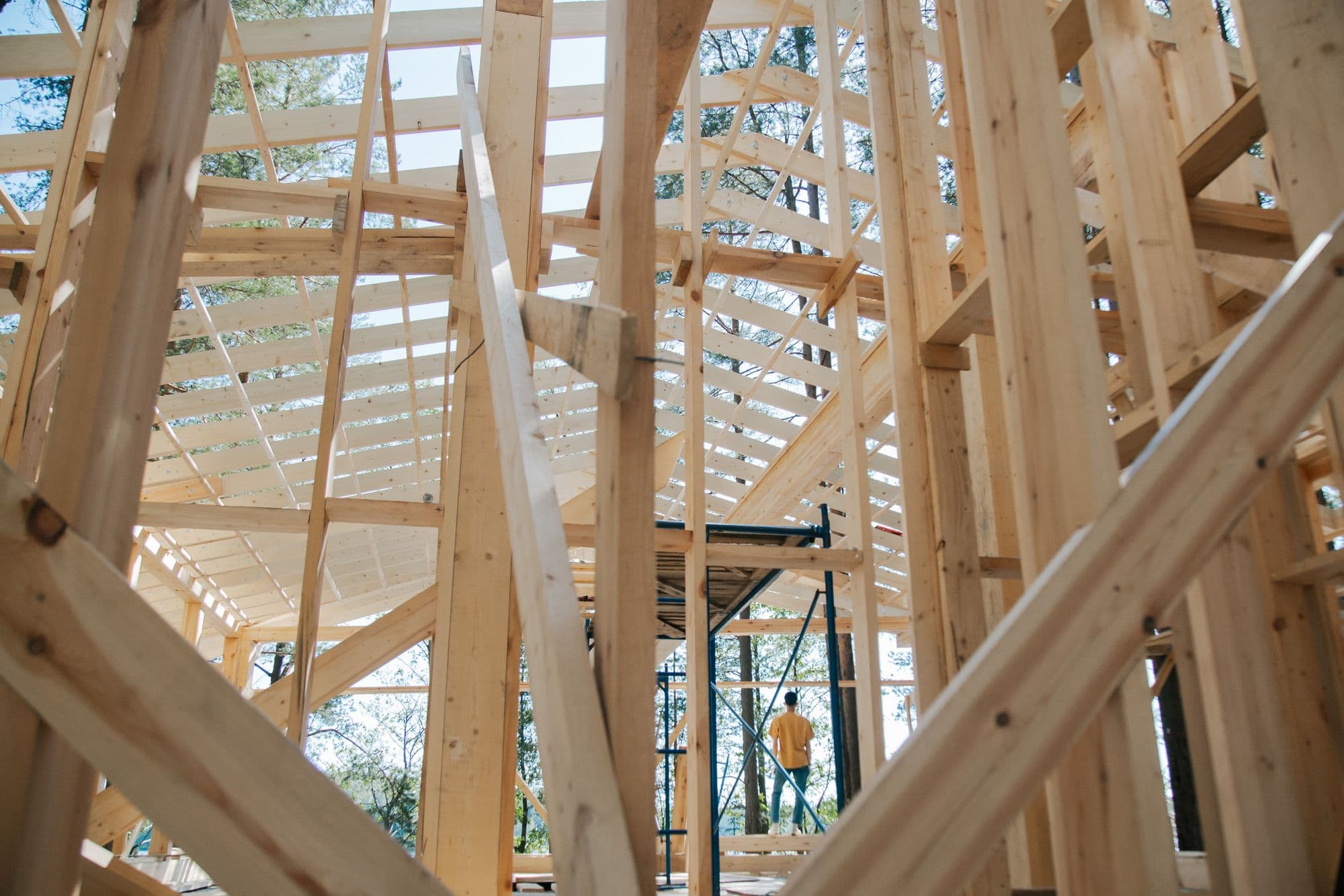Looking up through fresh timber framing and roof rafters, with a carpenter on the scaffold in the distance