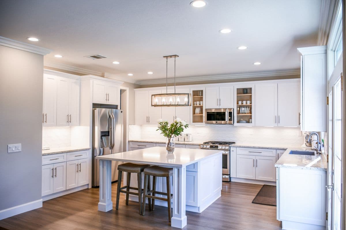 Finished white shaker kitchen with a center island, two stools, a lantern pendant and wide-plank floors