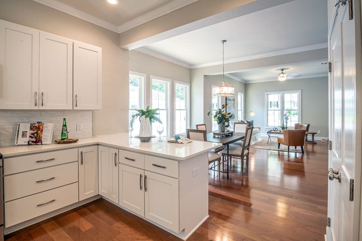 White kitchen peninsula opening onto a dining room with hardwood floors