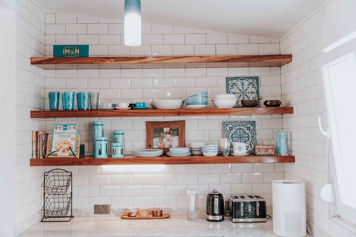 Open walnut shelves on a white subway tile wall, stocked with dishes and cookbooks