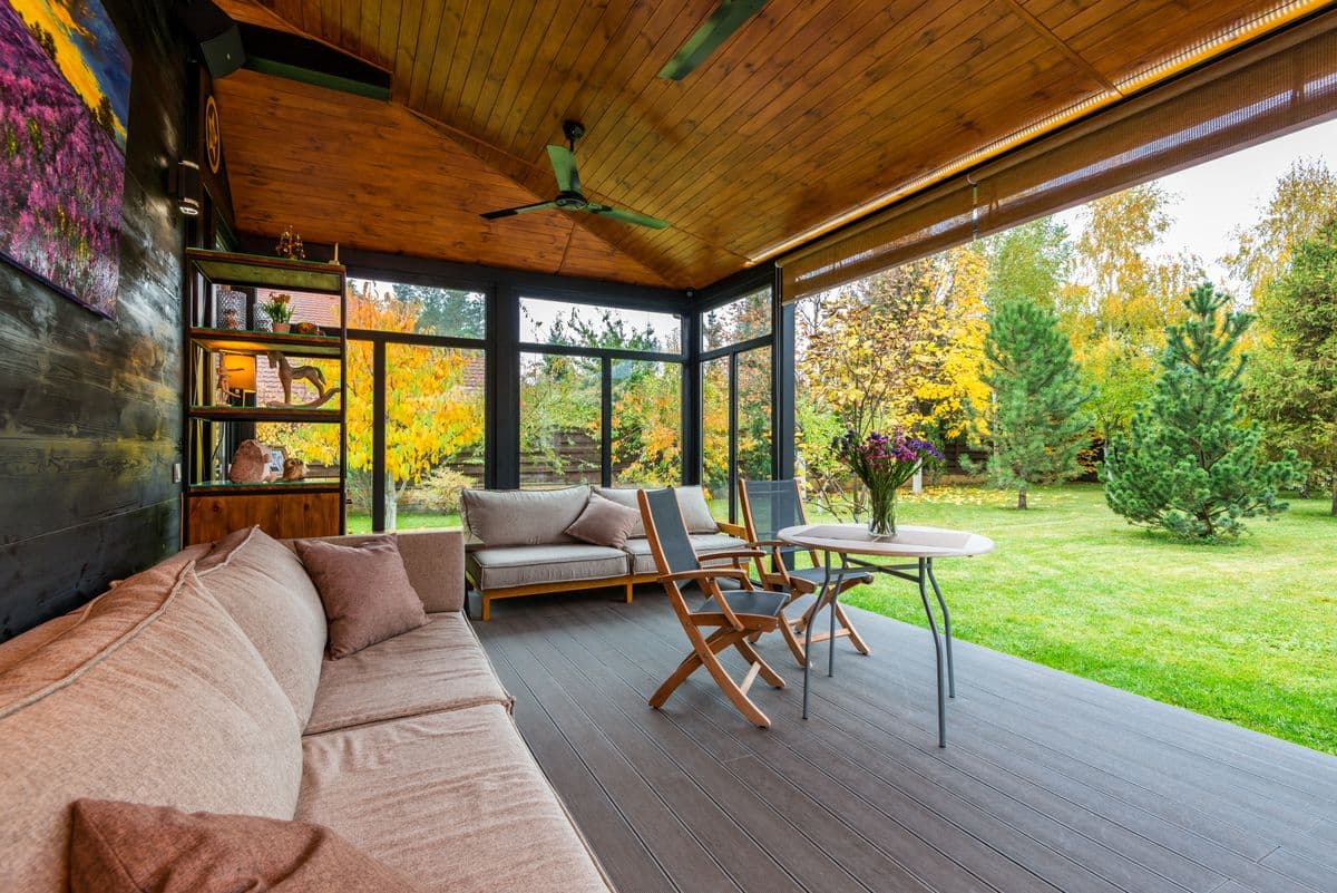 Screened porch with a tongue-and-groove wood ceiling, ceiling fan, sofa and dining set facing the lawn