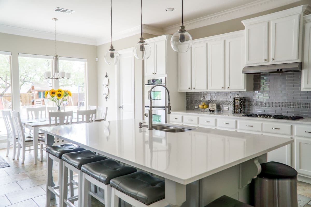 Bright white kitchen with a long quartz island, pendant lights and a dining nook by the windows