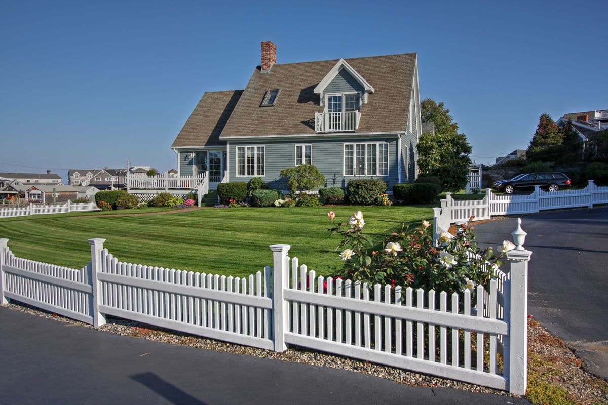 New England cape with a white picket fence, rose bushes and a freshly cut lawn