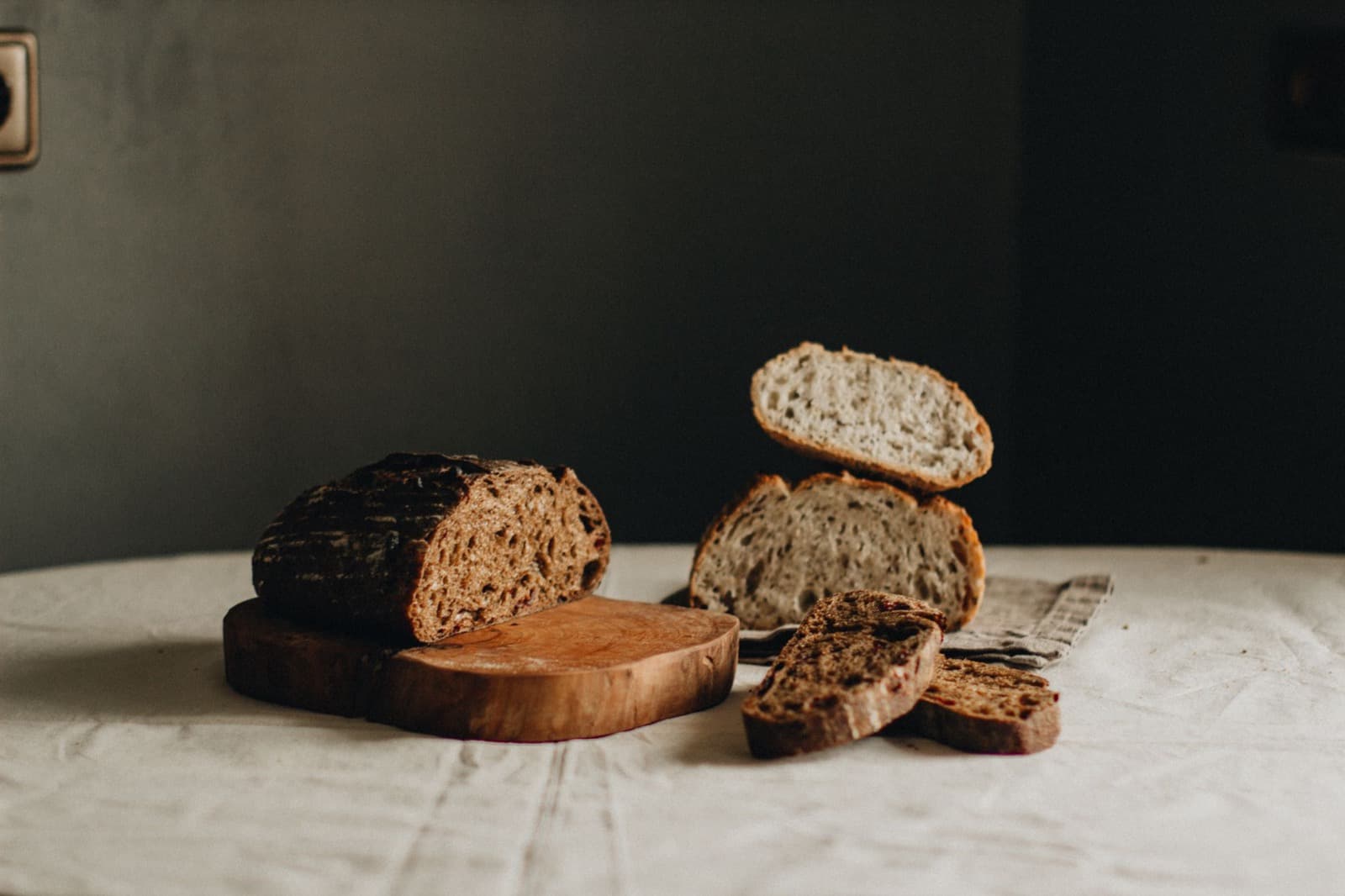 A dark-crusted rye loaf and thick slices on a cutting board against a deep shadow