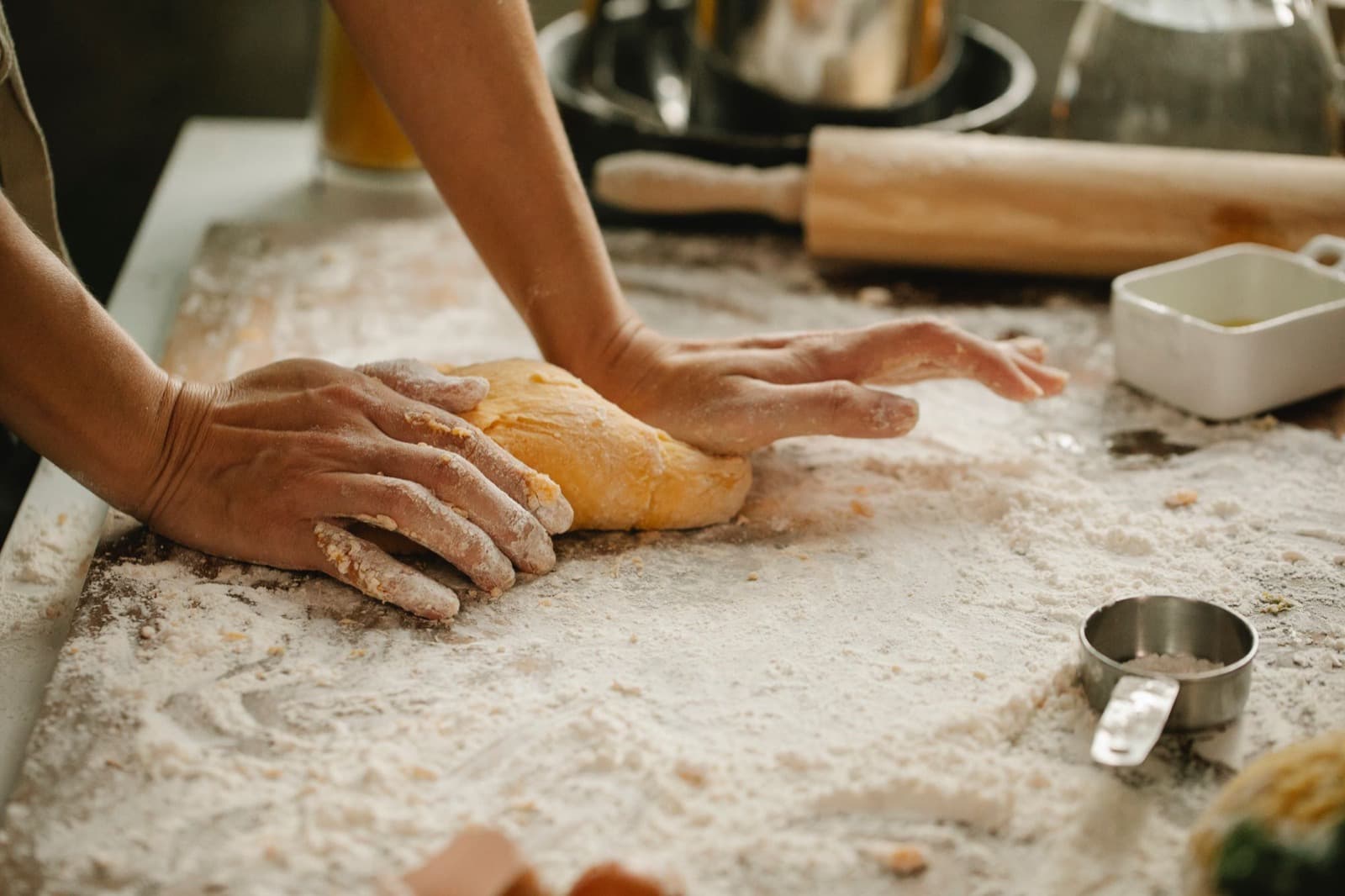 Hands kneading dough on a flour-covered counter beside a rolling pin