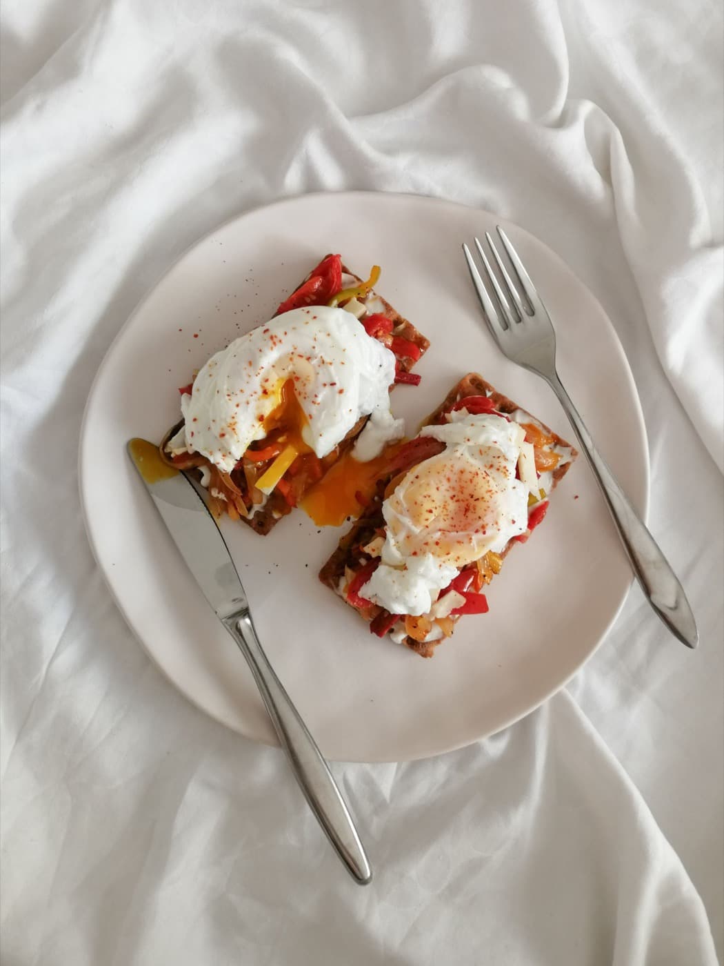 Two fried eggs on toast with tomato on a white plate set on rumpled linen