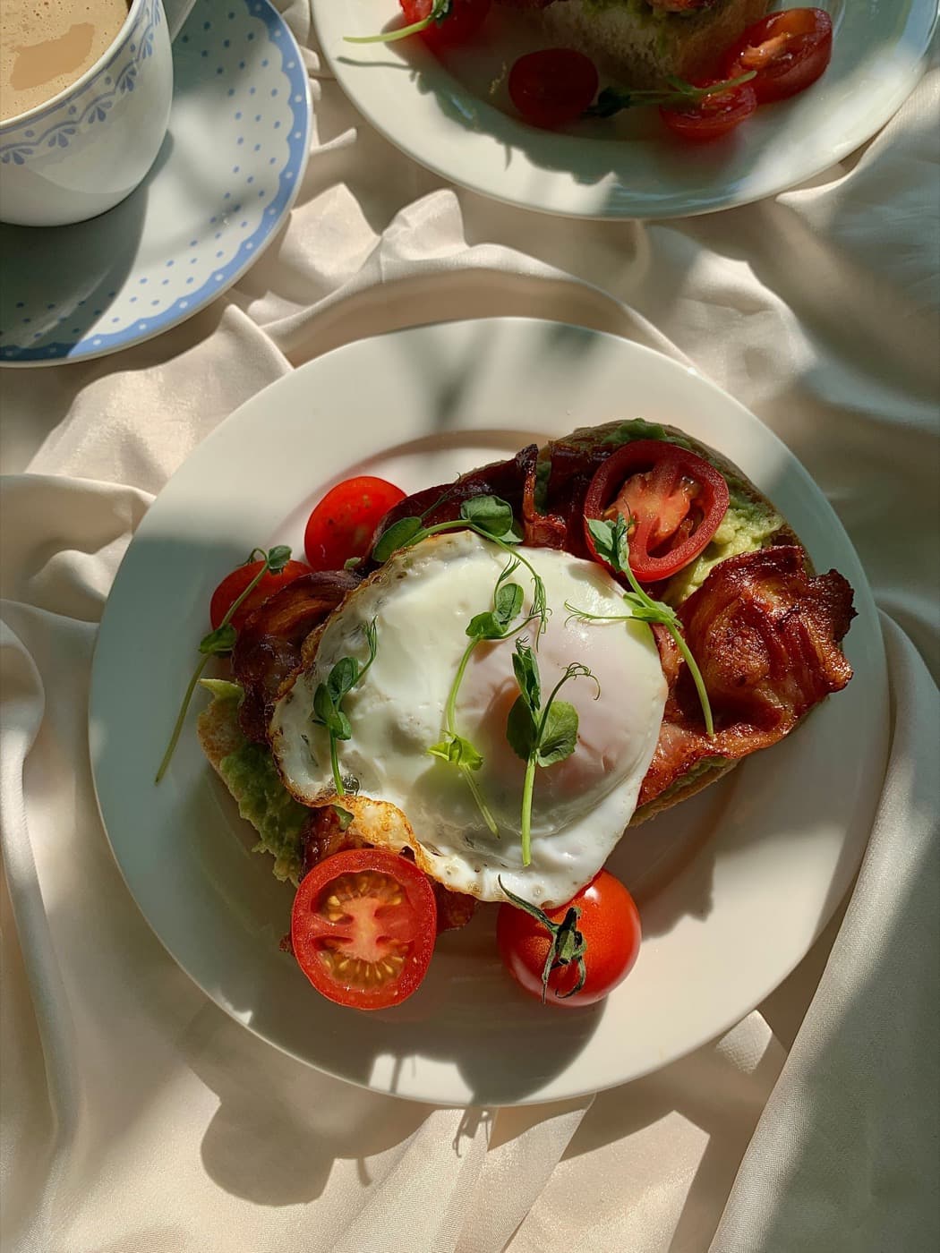 A soft egg, crisp bacon and roasted tomatoes on toast in morning light