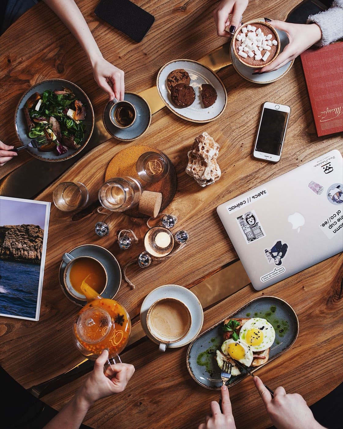 Overhead view of coworkers sharing coffee, eggs and pastries around a long wooden table
