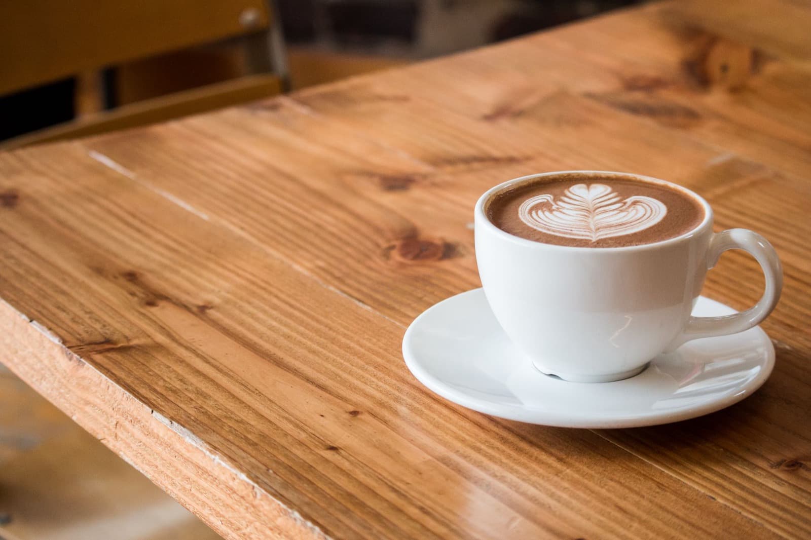 A latte with a rosetta in a white cup on a worn pine table