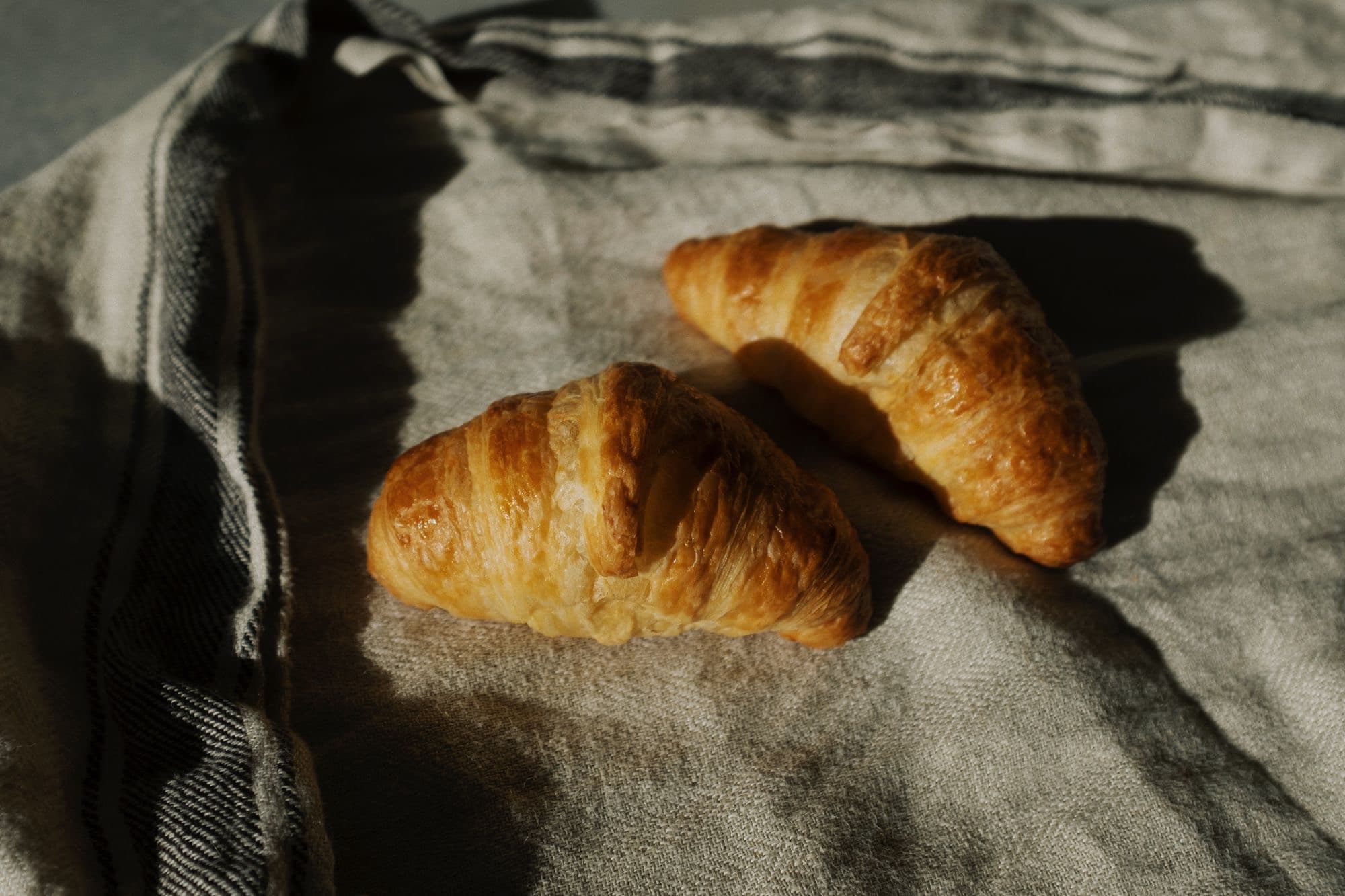 Two butter croissants in low morning sun on a striped linen cloth