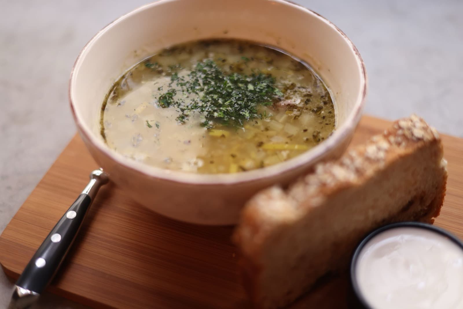 A bowl of chowder topped with herbs beside a thick slice of toasted bread on a board