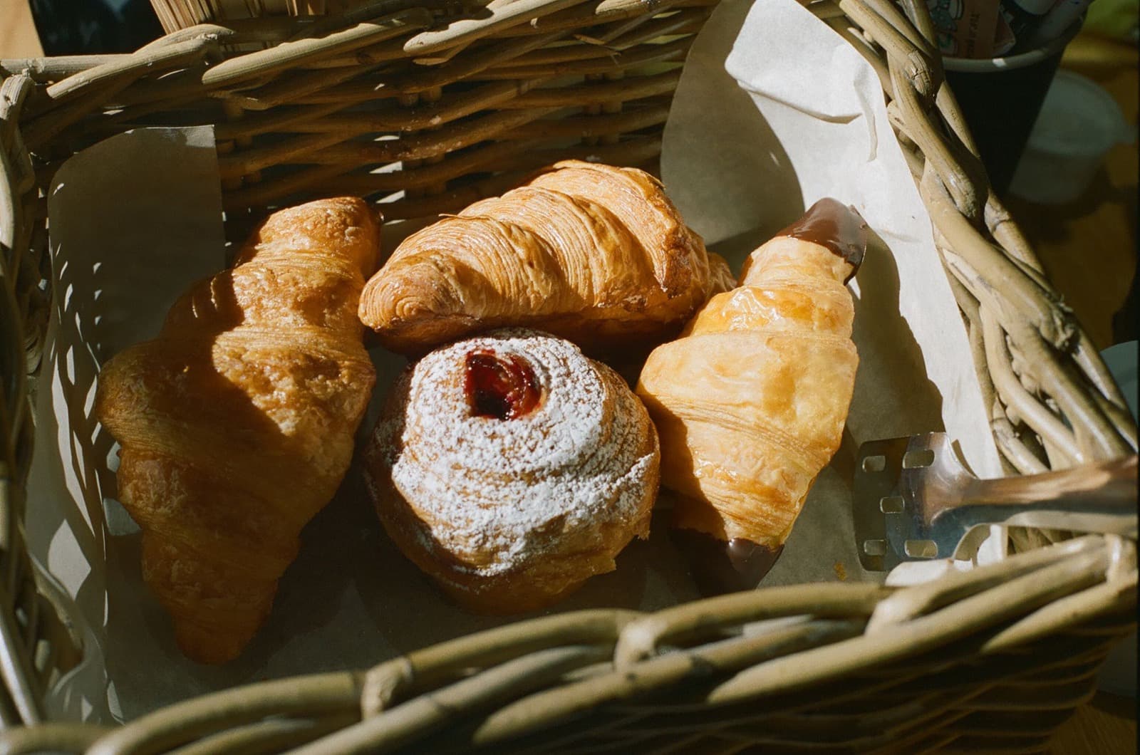 Croissants and a sugar-dusted bun in a woven wicker basket